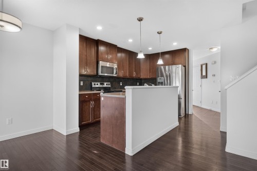 Wood-finish flooring throughout, kitchen with dark wood cabinetry, stainless steel appliances, pendant lighting, and recessed lighting - 2145 28 Street Nw, Edmonton, AB 