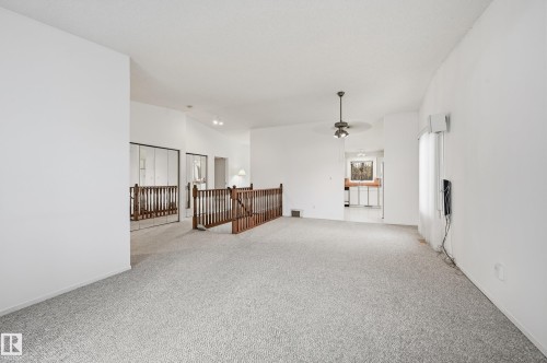 Open interior space featuring neutral carpeting, a wood-railed staircase, mirrored closet doors, and a ceiling-mounted light fixture with a fan - #19 10 Grange Dr, St. Albert, AB 
