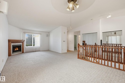 Open interior space featuring a wood-mantel fireplace, vaulted ceilings, multi-pane window, and wooden staircase railing with balusters - #19 10 Grange Dr, St. Albert, AB 