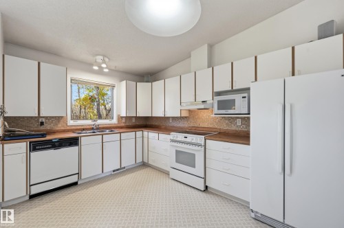 Kitchen featuring white cabinetry, wood-finish countertops, tile backsplash, white appliances, and patterned flooring - #19 10 Grange Dr, St. Albert, AB 