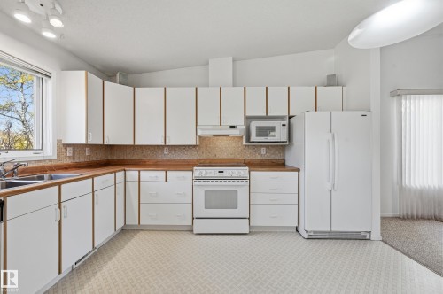 Kitchen featuring white cabinetry with wood detailing, wood-finish countertops, tile backsplash, built-in range, and dual-basin sink - #19 10 Grange Dr, St. Albert, AB 