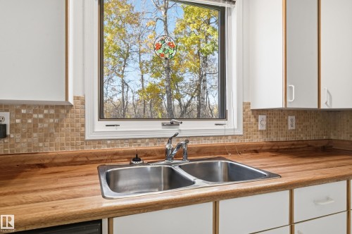 Kitchen featuring a natural wood countertop, dual-basin stainless steel sink, tiled mosaic backsplash, and white cabinetry - #19 10 Grange Dr, St. Albert, AB 