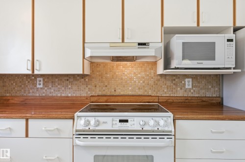 Kitchen featuring white flat-panel cabinetry, wood-finish countertops, glass mosaic tile backsplash, built-in range, and integrated range hood - #19 10 Grange Dr, St. Albert, AB 