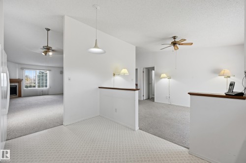 Interior space featuring wall-mounted lighting fixtures, hanging pendant lighting, ceiling fans, and a fireplace with a wood-finish mantel - #19 10 Grange Dr, St. Albert, AB 