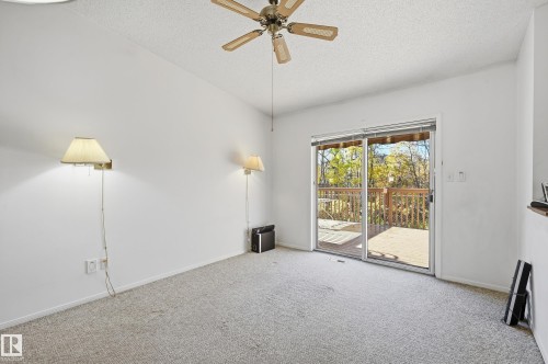 Room featuring neutral wall-to-wall carpeting, a ceiling fan, dual wall-mounted light fixtures, and a sliding glass door providing external access to a wooden deck - #19 10 Grange Dr, St. Albert, AB 