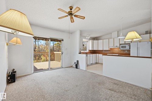Open-concept kitchen featuring white cabinetry, a peninsula breakfast bar, and a sliding glass door opening to a wooden deck - #19 10 Grange Dr, St. Albert, AB 