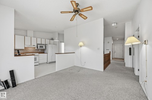 Kitchen featuring white cabinetry, integrated appliances, and a pass-through counter, accompanied by wall-mounted lighting and a ceiling fan with wood-finish blades - #19 10 Grange Dr, St. Albert, AB 