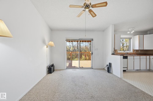 Open-concept interior featuring sliding glass doors to a wooden deck, kitchen cabinetry with neutral-toned countertops, and a ceiling fan - #19 10 Grange Dr, St. Albert, AB 
