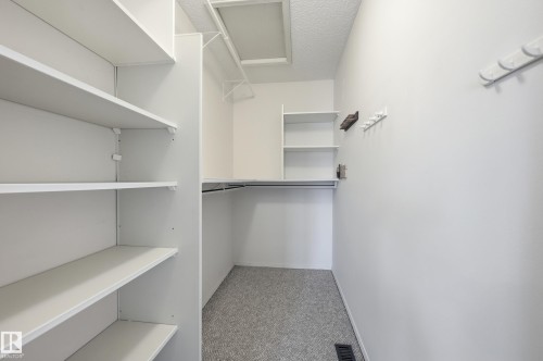 Walk-in closet featuring floor-to-ceiling built-in shelving, integrated hanging rods, and neutral carpeting - #19 10 Grange Dr, St. Albert, AB 