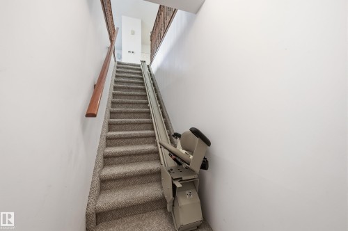 Staircase featuring wall-to-wall carpeting, wood handrail, decorative metal balusters, and a motorized stair lift - #19 10 Grange Dr, St. Albert, AB 