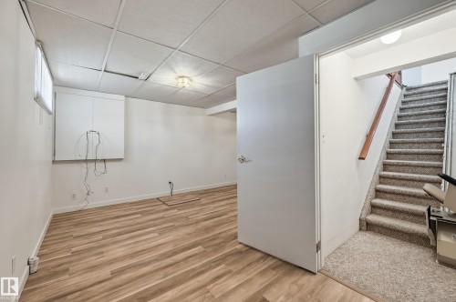 Wood-finish flooring, drop ceiling with flush-mount lighting, built-in wall cabinetry, and carpeted staircase with wood handrail - #19 10 Grange Dr, St. Albert, AB 