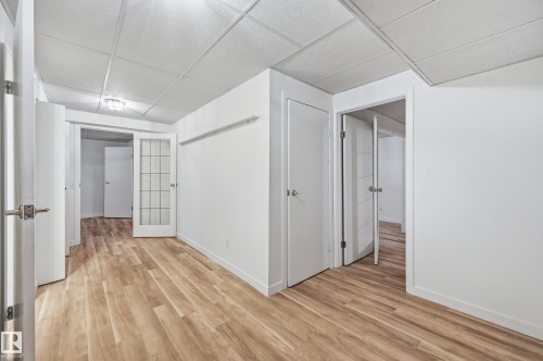 Interior space featuring wood-finish flooring, drop ceiling panels, multi-panel doors, and a glass-paneled interior door - #19 10 Grange Dr, St. Albert, AB 