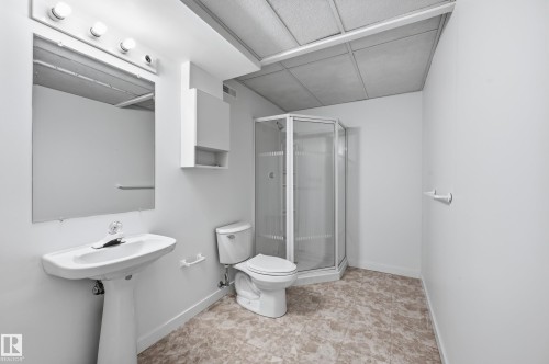Bathroom featuring a white pedestal sink, corner shower with frosted glass enclosure, wall-mounted medicine cabinet, and patterned tile flooring - #19 10 Grange Dr, St. Albert, AB 
