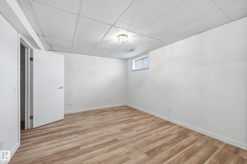 Interior space featuring wood-finish flooring, a white-paneled drop ceiling with a central light fixture, a small inset window, and a built-in closet with a swing door - #19 10 Grange Dr, St. Albert, AB 