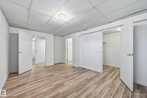 Room featuring wood-finish flooring, drop ceiling with flush-mount lighting, and multiple interior doorways with reach-in closet storage - #19 10 Grange Dr, St. Albert, AB 