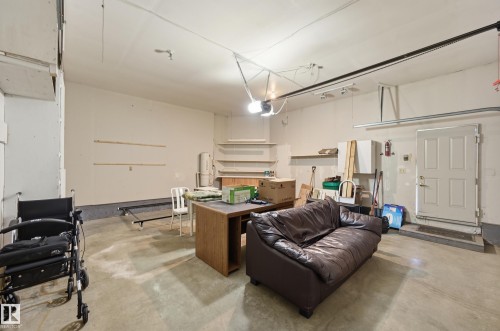 Garage space featuring concrete flooring, built-in shelving, an automated overhead door opener, and a dedicated exterior access door - #19 10 Grange Dr, St. Albert, AB 