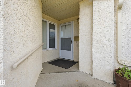 Stucco exterior entryway featuring a concrete porch, a metal handrail, a storm door with glass paneling, and an attached mailbox - #19 10 Grange Dr, St. Albert, AB 