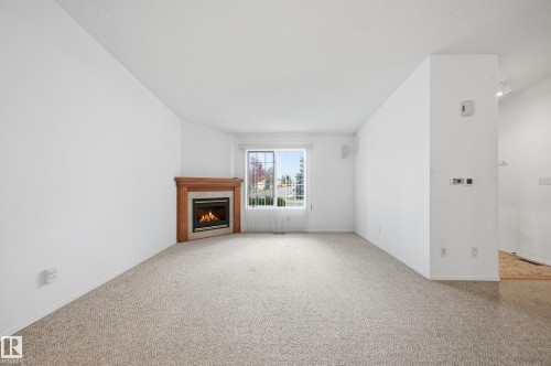 Corner fireplace featuring a wood mantel and tile surround, carpeted flooring, and a large window - #19 10 Grange Dr, St. Albert, AB 