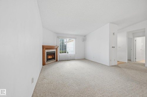 Living area featuring neutral carpeting, a corner fireplace with a wood mantel, and vertical blinds - #19 10 Grange Dr, St. Albert, AB 