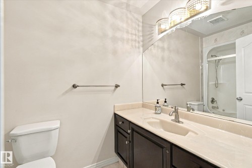 Vanity with integrated sink, dark wood-finish cabinetry, full-width mirror, and three-light fixture - 771 Johns Road Nw, Edmonton, AB 