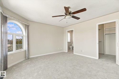 Arched window with upper transom, wall-to-wall carpeting, ceiling fan with integrated lighting, built-in closet shelving, and a permanent door leading to a separate area - 771 Johns Road Nw, Edmonton, AB 