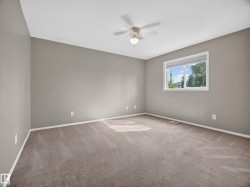 Neutral-toned walls with a white-framed window, overhead ceiling fan with lighting, and plush carpeting - 