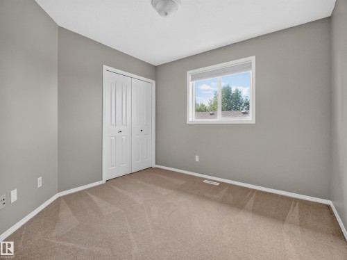 Neutral wall paint, carpet flooring, window with white trim, and bi-fold closet doors - 14 Wells Court, Leduc, AB 