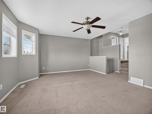 Spacious room with neutral gray walls, two windows, and a ceiling fan with integrated lighting - 14 Wells Court, Leduc, AB 