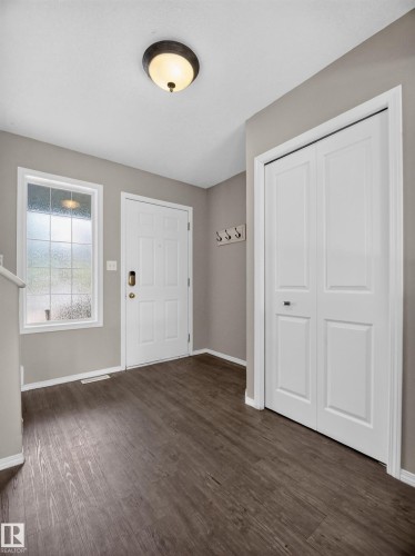 Entryway featuring wood-finish flooring, a contemporary flush-mount ceiling light, a white paneled door, and a frosted glass window - 14 Wells Court, Leduc, AB 
