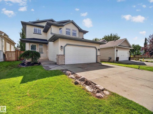 Two-story exterior with light-toned siding, attached two-car garage, concrete driveway, and a manicured lawn - 14 Wells Court, Leduc, AB 
