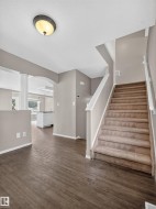 Wood-finish flooring, staircase with carpeting, recessed ceiling light, white trim, and a partial view of a kitchen with white cabinetry - 