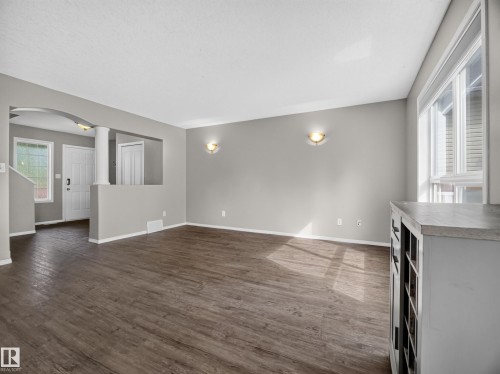 Spacious main living area featuring wood-finish flooring, neutral paint palette, ample natural light from large windows, and an arched entry - 14 Wells Court, Leduc, AB 