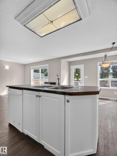 Kitchen island featuring white cabinetry, a double basin sink, and a dishwasher - 14 Wells Court, Leduc, AB 