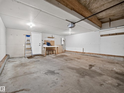 Concrete flooring throughout, exposed wood ceiling beams, overhead garage door opener, and a white service door - 14 Wells Court, Leduc, AB 