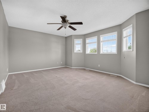 Spacious room with a ceiling fan, light gray wall paint, multiple windows with blinds, and beige carpeting - 14 Wells Court, Leduc, AB 