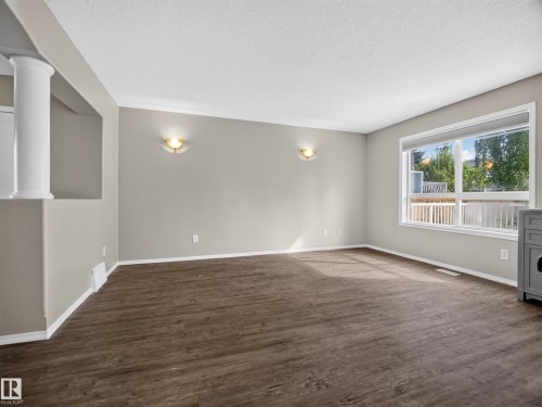 Expansive room featuring wood-finish flooring, neutral paint, a large window, and decorative wall sconces - 14 Wells Court, Leduc, AB 