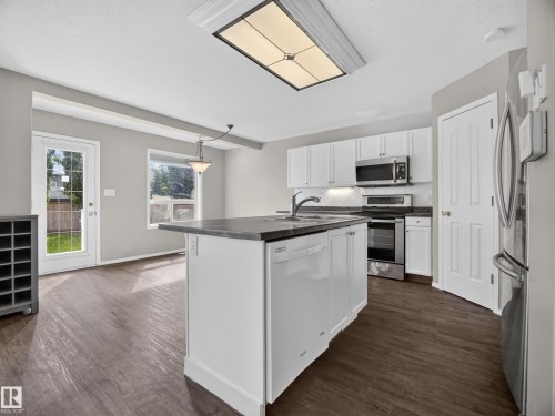 Kitchen featuring white cabinetry, stainless steel appliances, dark countertops, and wood-finish flooring - 14 Wells Court, Leduc, AB 