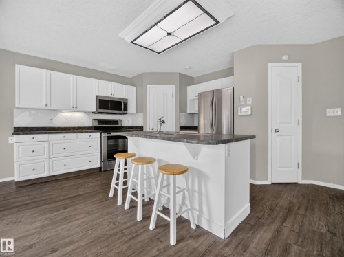 Kitchen featuring white cabinetry, stainless steel appliances, dark countertops, and wood-finish flooring - 14 Wells Court, Leduc, AB 