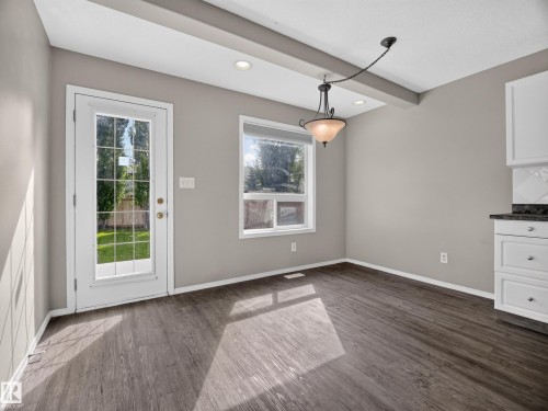 Wood-finish flooring, recessed ceiling lighting, decorative ceiling beam, white cabinetry with dark countertops, and a glass-paned exterior door - 14 Wells Court, Leduc, AB 