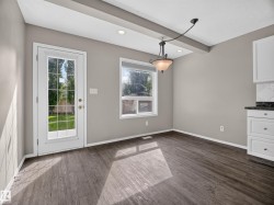 Wood-finish flooring, recessed ceiling lighting, decorative ceiling beam, white cabinetry with dark countertops, and a glass-paned exterior door - 