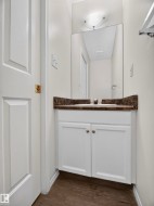 White vanity cabinetry with a dark stone-finish countertop, undermount sink, and wood-finish flooring - 