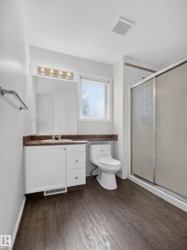 Wood-finish flooring, white vanity with integrated sink, toilet, and a glass-enclosed shower - 14 Wells Court, Leduc, AB 