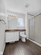 Wood-finish flooring, white vanity with integrated sink, toilet, and a glass-enclosed shower - 