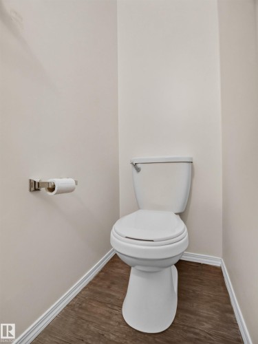 Wood-finish flooring with white trim, a white toilet, and a brushed nickel toilet paper holder - 14 Wells Court, Leduc, AB 