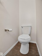 Wood-finish flooring with white trim, a white toilet, and a brushed nickel toilet paper holder - 