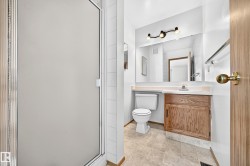 Frosted glass shower enclosure, wood-finish vanity with countertop, large wall-mounted mirror, and tile flooring - 