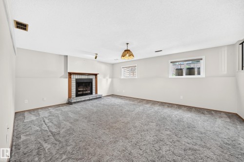 Spacious living area featuring neutral carpeting, recessed ceiling lighting, and a brick fireplace with dark surround - 14519 32 Street Nw, Edmonton, AB 