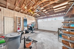 Concrete flooring garage with exposed ceiling joists, wood paneling, and a white paneled garage door with upper-row windows - 