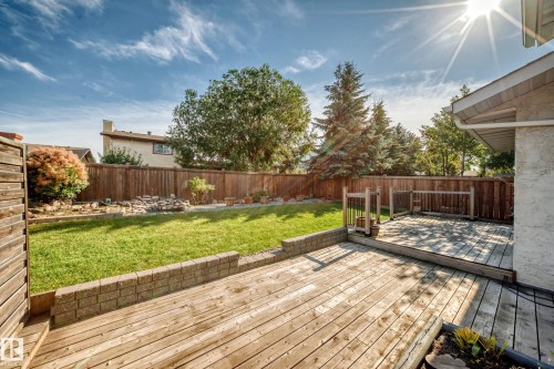 Expansive backyard oasis featuring a composite deck with clean lines, manicured lawn, mature landscaping including evergreen and deciduous trees, and retaining wall borders - 14519 32 Street Nw, Edmonton, AB 