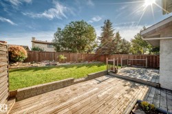 Expansive backyard oasis featuring a composite deck with clean lines, manicured lawn, mature landscaping including evergreen and deciduous trees, and retaining wall borders - 